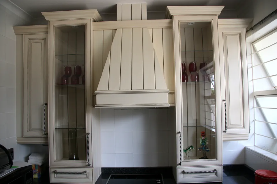 Painted country kitchen with a timber canopy hood between leaded glass cabinets