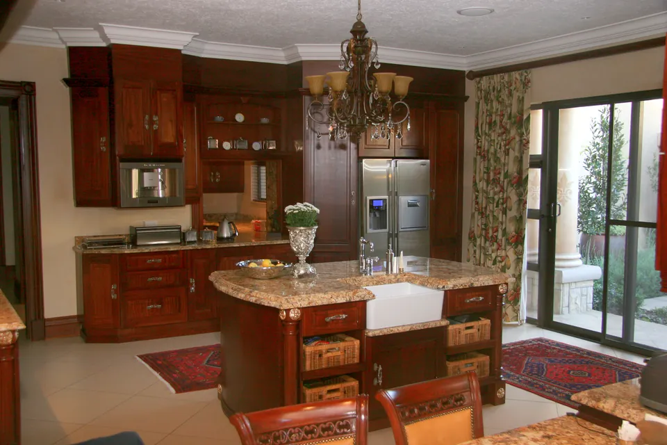 Mahogany kitchen with a central island under a chandelier and doors out to the garden