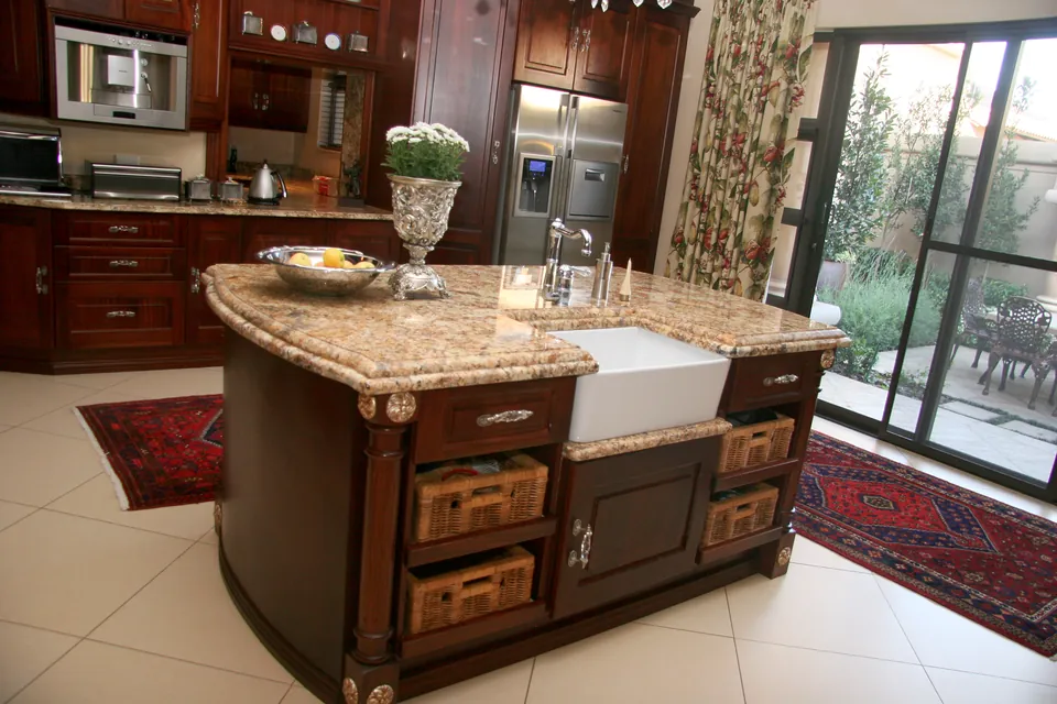 Kitchen island in solid African mahogany with a granite top, farmhouse sink and woven drawer baskets
