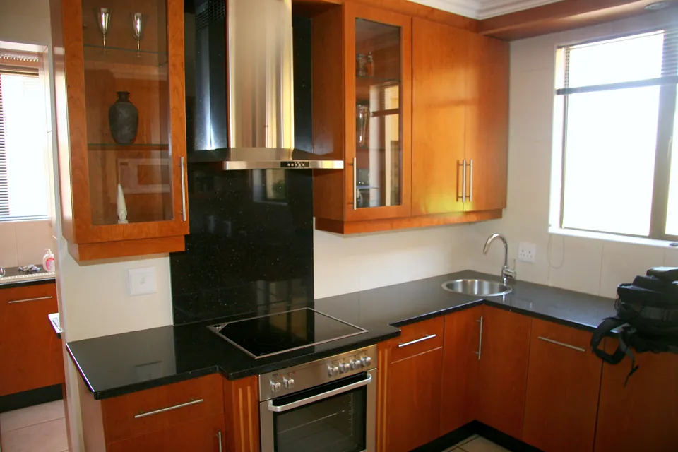 Cherry veneer kitchen with black stone tops and a black glass splashback