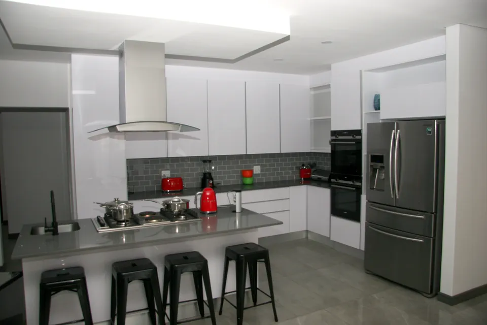 White gloss kitchen with an island, grey stone tops and a grey subway-tile splashback