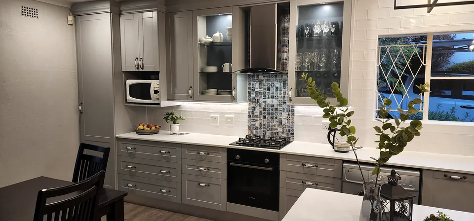 Shaker kitchen in a soft grey painted finish with a patterned splashback and lit glazed cabinets
